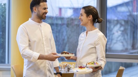 Zwei Kellner tauschen Lächeln beim Servieren von Speisen in einem Restaurant