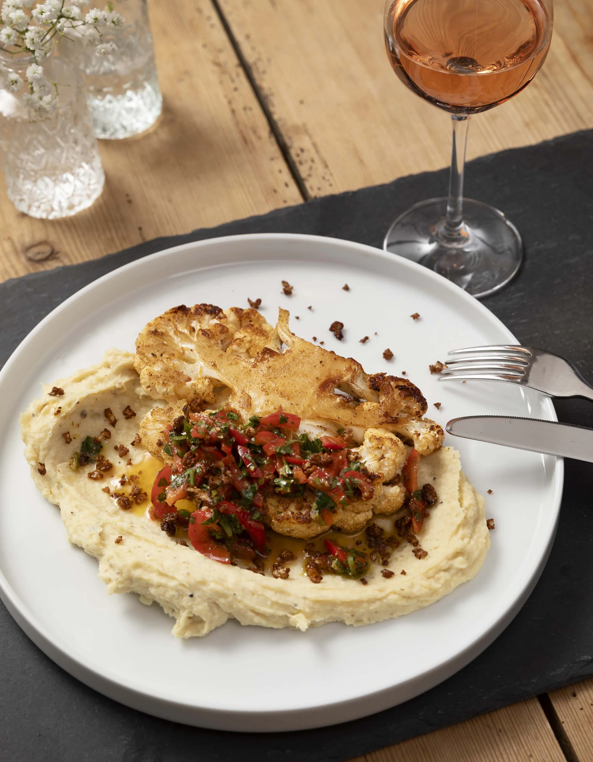 Gebackener Blumenkohl mit Creme und Kräutern auf weißem Teller mit Glas Roséwein