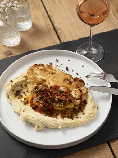 Bayerisches Restaurant nahe Augsburg gesucht? Gebackener Blumenkohl mit Creme und Kräutern auf weißem Teller mit Glas Roséwein