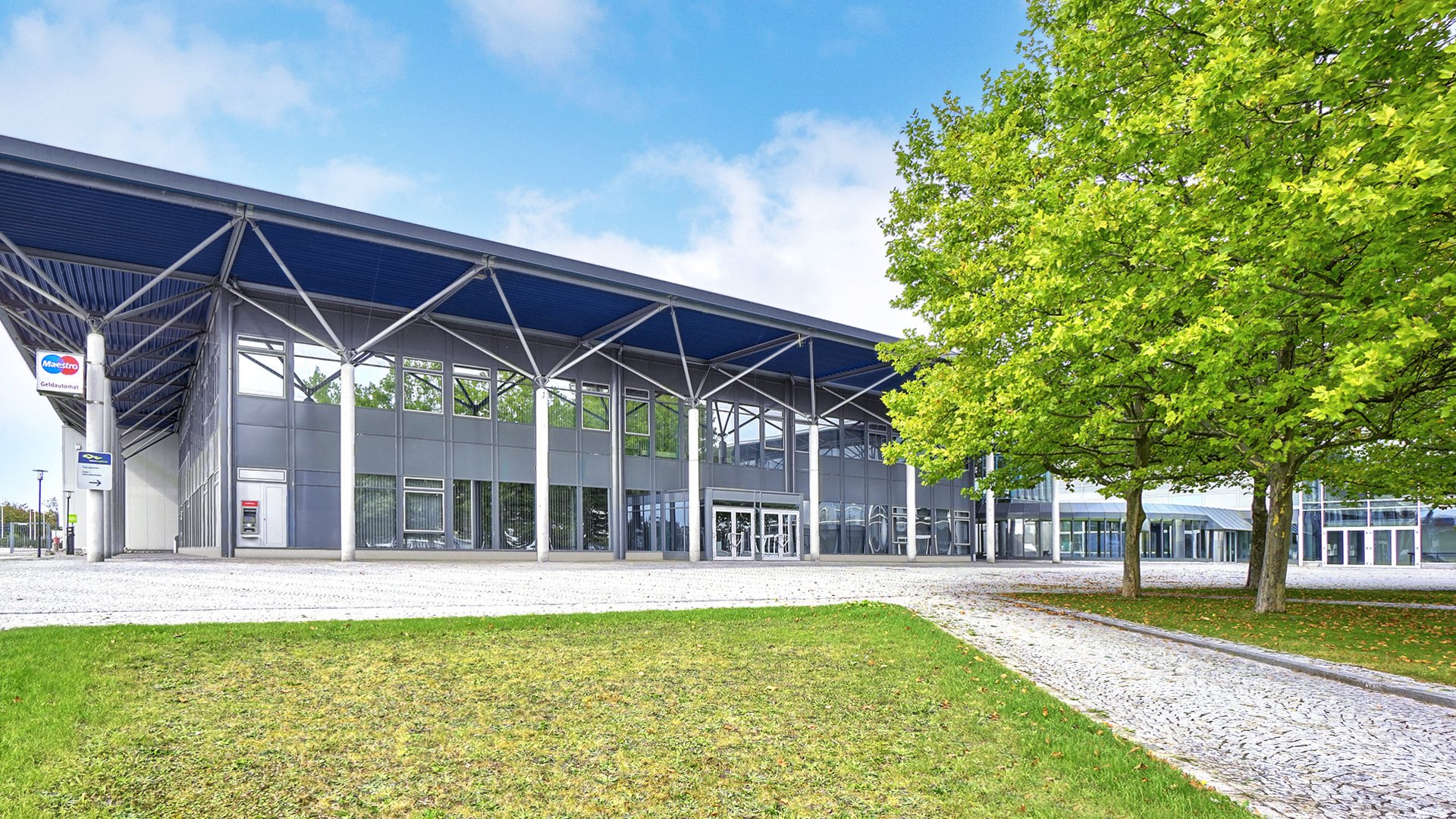 Moderner Gebäudekomplex mit Glasfassade und Grünfläche bei blauem Himmel