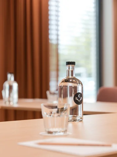Zeller’s Quartier: das besondere Tagungshotel in Bayern Tagungstisch mit Wasserflasche, Wasserglas, Block und Stift.