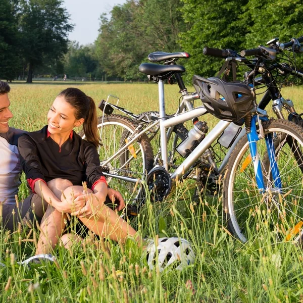Couple sitting on grass next to bicycles on a sunny day