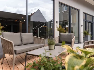 Loungesitzgruppe auf der Holzterrasse Lounge-Sitzgruppe auf der Holzterrasse vor dem Zeller’s Quartier mit Glasfassade und bepflanztem Außenbereich.