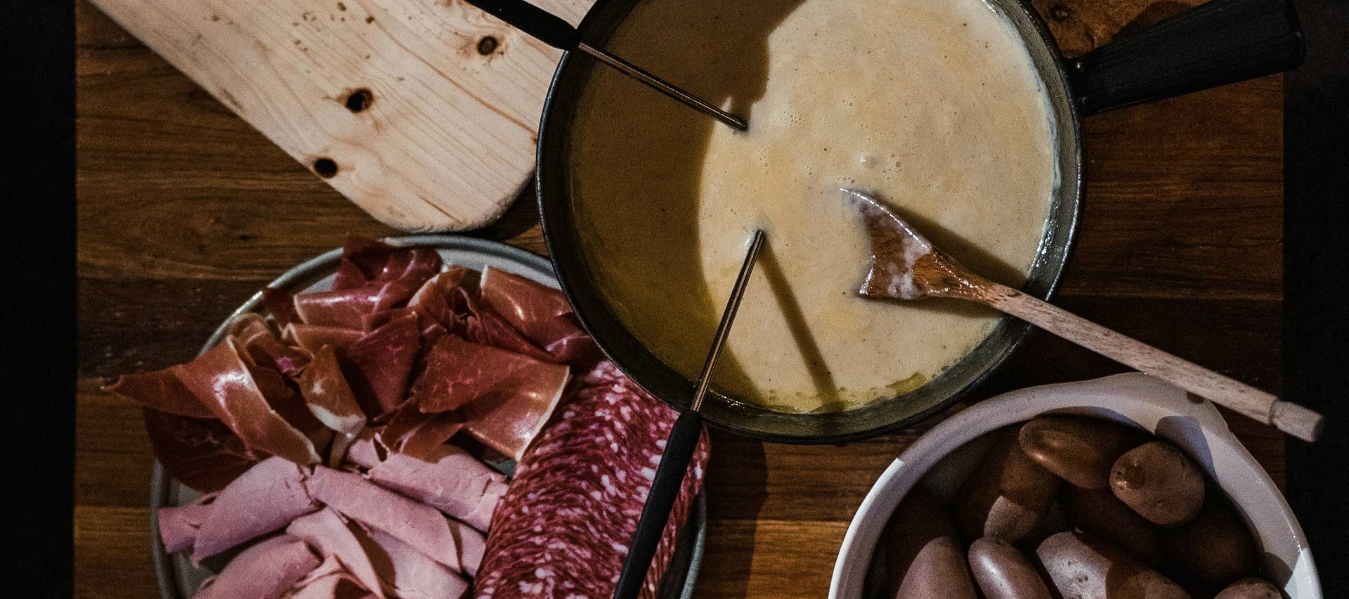 Fondue-Set mit Käse, Brot, Salat, Kartoffeln und Aufschnitt auf Holztisch