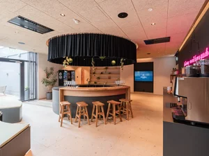 Zeller’s Quartier: das besondere Tagungshotel in Bayern Moderner Barbereich mit Holzstühlen, rundem Tresen und schwarzem Vorhang an der Decke
