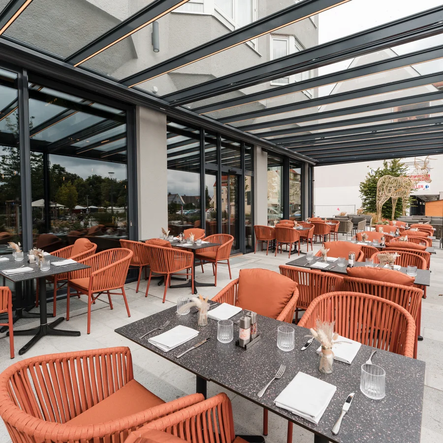 Cervus: das Restaurant in Königsbrunn mit dem gewissen Extra Außenbereich eines Restaurants mit roten Stühlen und eingedeckten Tischen unter Glasdach