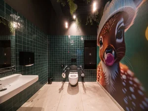 Toilette in der Lobby Barrierefreies Badezimmer mit grün gefliesten Wänden und Wandbild eines Rehkitzes