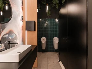 Lobbytoilette Moderne Lobby-Toilette im Zeller’s Quartier mit Waschbecken, dunklen Kabinen, Urinalen und grünen Wandfliesen.