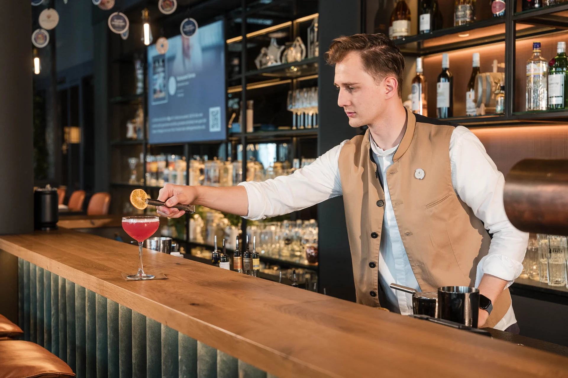 Cervus: the restaurant in Königsbrunn with special flair Mitarbeiter steht hinter der Bar im Restaurant Cervus mit Cocktails, Holztheke und Spirituosenregal im Hintergrund.