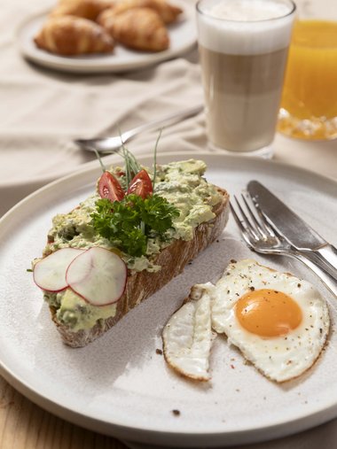 Toast mit Avocadocreme, Spiegelei, Croissants, Latte Macchiato und Orangensaft
