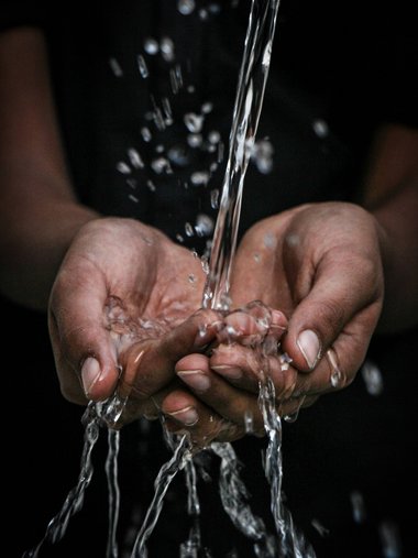 Water flowing into cupped hands against dark background