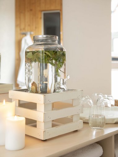 Water dispenser with herbs and candles on wooden table in spa setting
