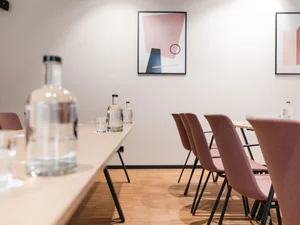 Zeller’s Quartier: das besondere Tagungshotel in Bayern Konferenzraum mit rosa Stühlen, Flaschen und abstrakten Bildern an der Wand