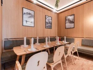 Südtiroler Stube Heller Restaurantbereich im Cervus mit gedeckten Holztischen, Stühlen, Sitzbank und Bildern an der Wand.