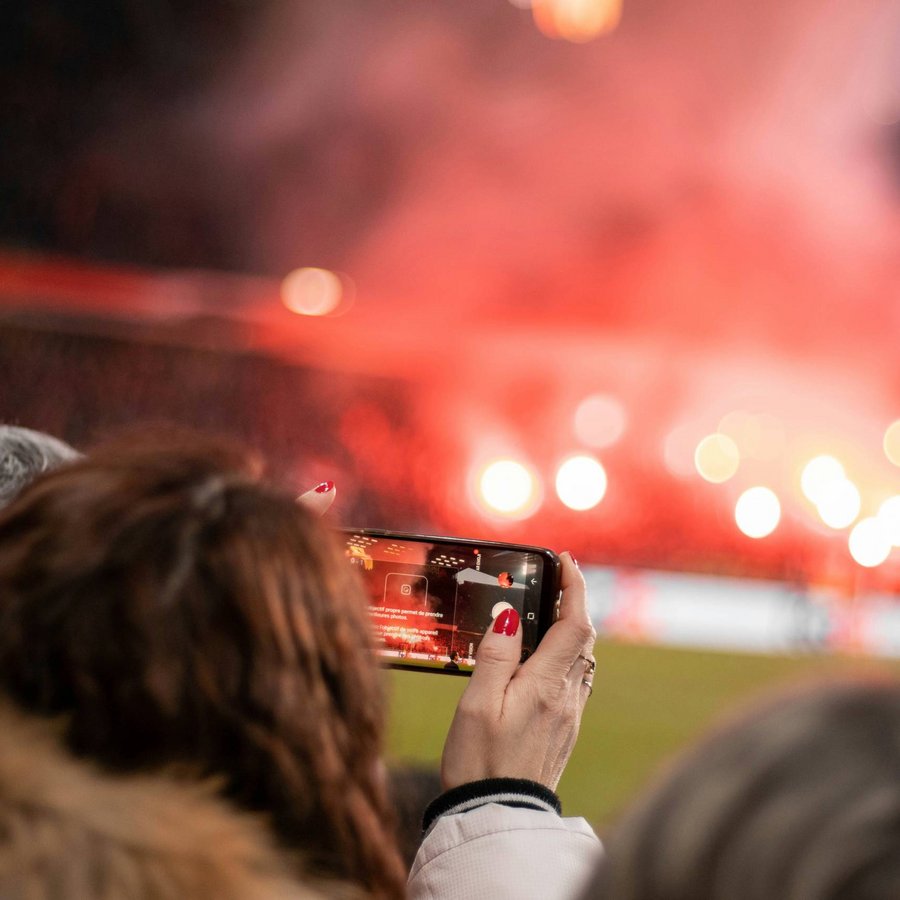 Entfernung von Zeller’s Quartier: Person filmt rot leuchtendes Feuerwerk auf einem Sportplatz mit dem Smartphone