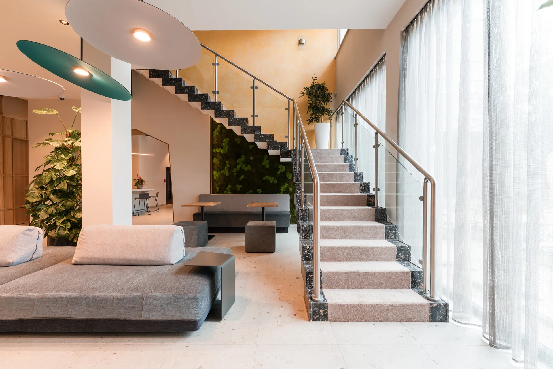 Moderner Wohnbereich mit grauer Couch und Treppe mit Teppich und Glasgeländer
