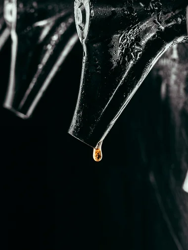 Nahaufnahme eines schwarzen Wasserhahns mit einem orangefarbenen Tropfen