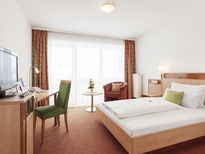 Hell eingerichtetes Hotelzimmer mit Einzelbett, Fernseher und Schreibtisch