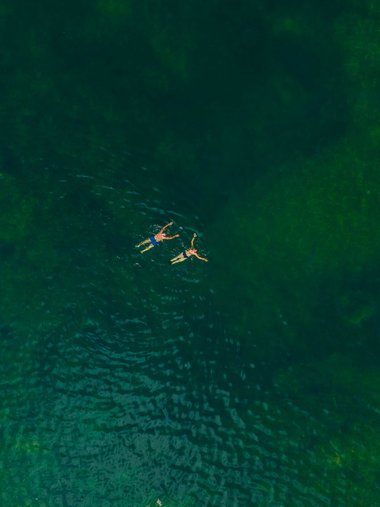Two swimmers and two paddleboards on green water viewed from above