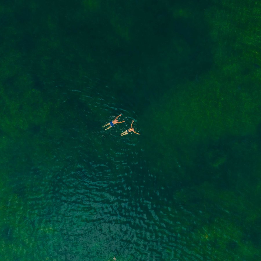 Egal, ob aktiv oder entspannt – Zwei Schwimmer und zwei Paddelboote auf grünem Wasser von oben gesehen