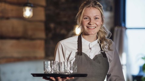 Lächelnde Kellnerin trägt Tablett mit Gläsern in gemütlichem Restaurant
