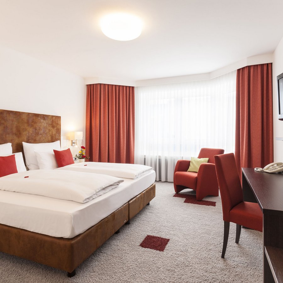 Schlafquartier Helles Hotelzimmer mit Doppelbett, roten Vorhängen und Sesseln