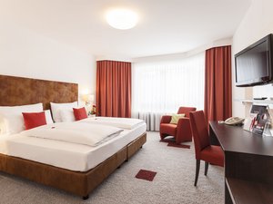 Helles Hotelzimmer mit Doppelbett, roten Vorhängen und Sesseln