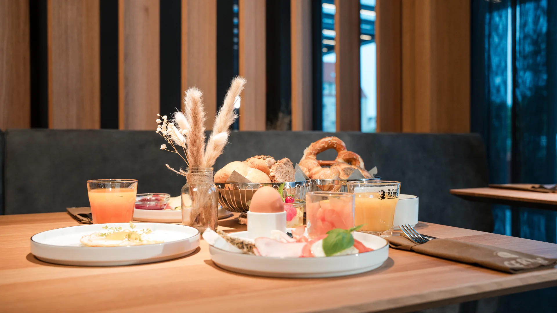 Breakfast table with bread rolls, egg, cold cuts, and orange juice in modern café
