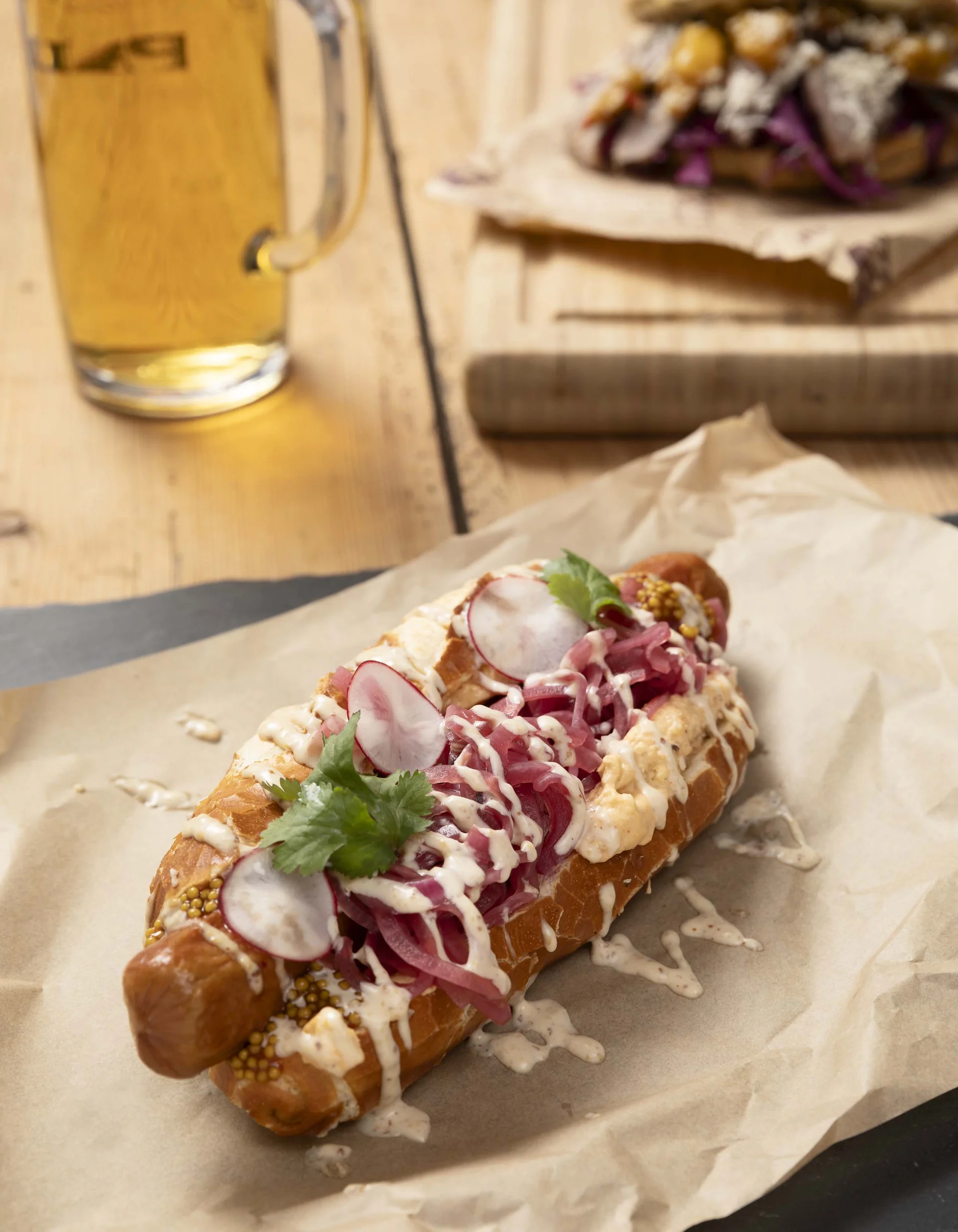 Würstchen im Brötchen mit Sauce, Radieschen und Bier im Hintergrund