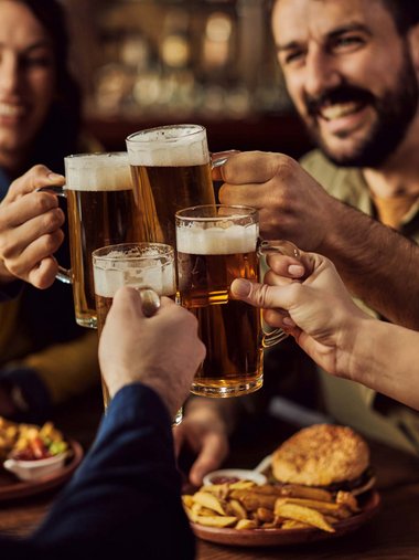 Friends clinking beer mugs in a restaurant with burgers and fries
