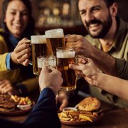 Group of friends clinking beer mugs in a bar with food on the table