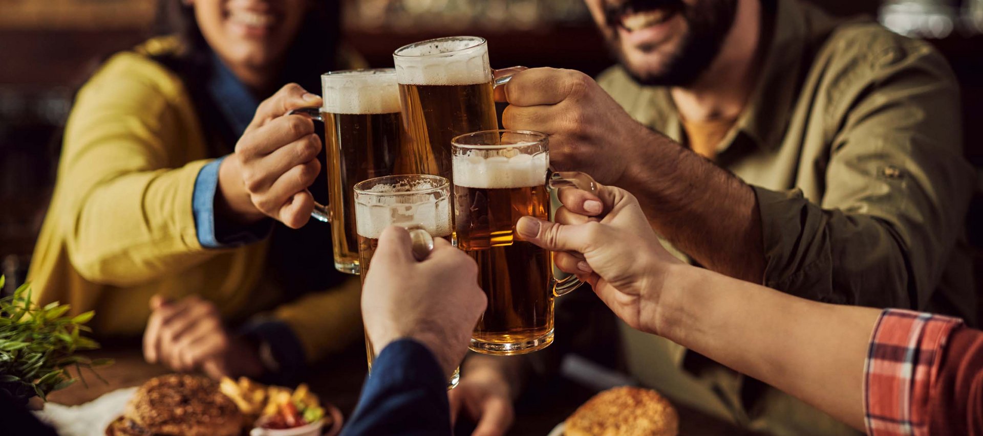 Gruppe von Freunden stößt mit Biergläsern in einer Bar an, Essen auf dem Tisch