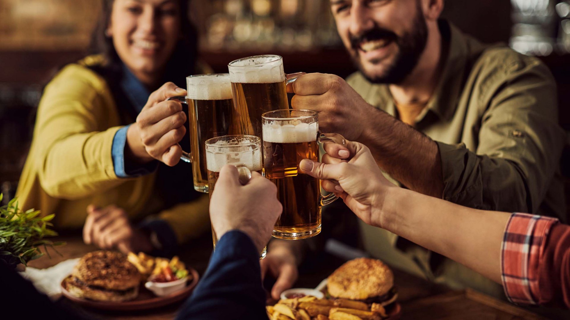 Gruppe von Freunden stößt mit Biergläsern in einer Bar an, Essen auf dem Tisch