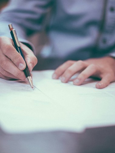 Person unterschreibt Dokument mit Stift auf Schreibtisch