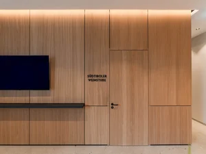 Eingang zur Südtiroler Stube Eingang zur Südtiroler Weinstube mit heller Holzverkleidung, Tür und Fernseher im Zeller’s Quartier.