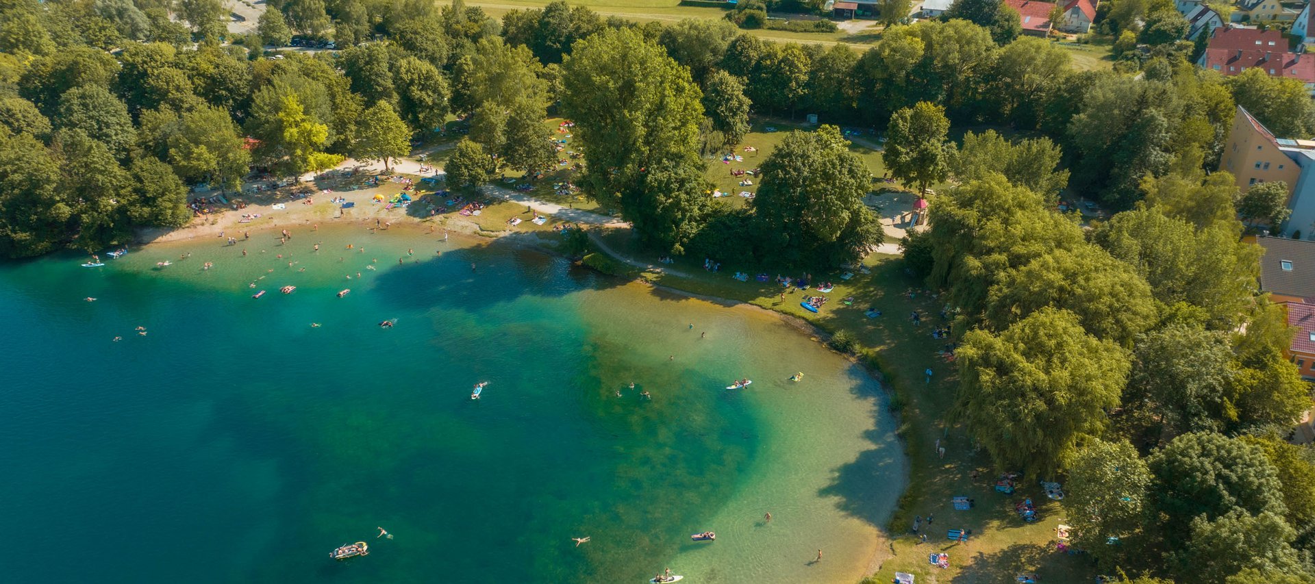 Aerial view of a busy lake with people swimming and relaxing on the surrounding green area