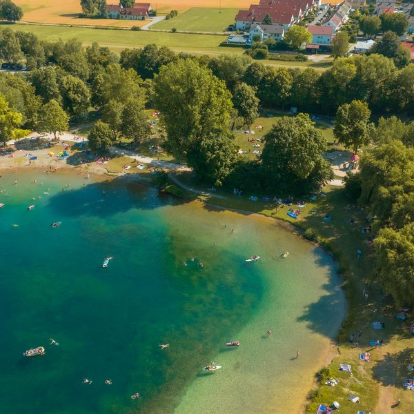 Überblick über einen belebten See mit Menschen im Wasser und auf dem angrenzenden Grünbereich