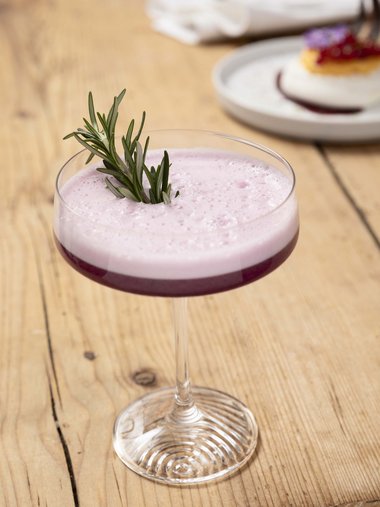Lila Cocktail mit Rosmarinzweig in einem Glas auf Holztisch