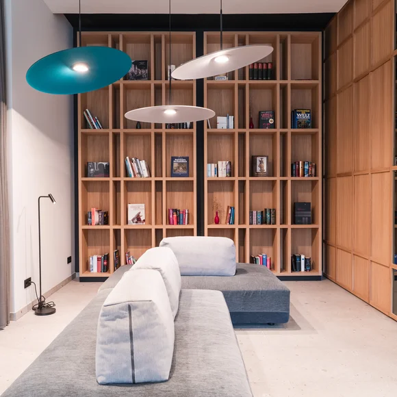 Moderner Wohnbereich mit grauem Sofa, Holzbücherregal und hängenden Lampen