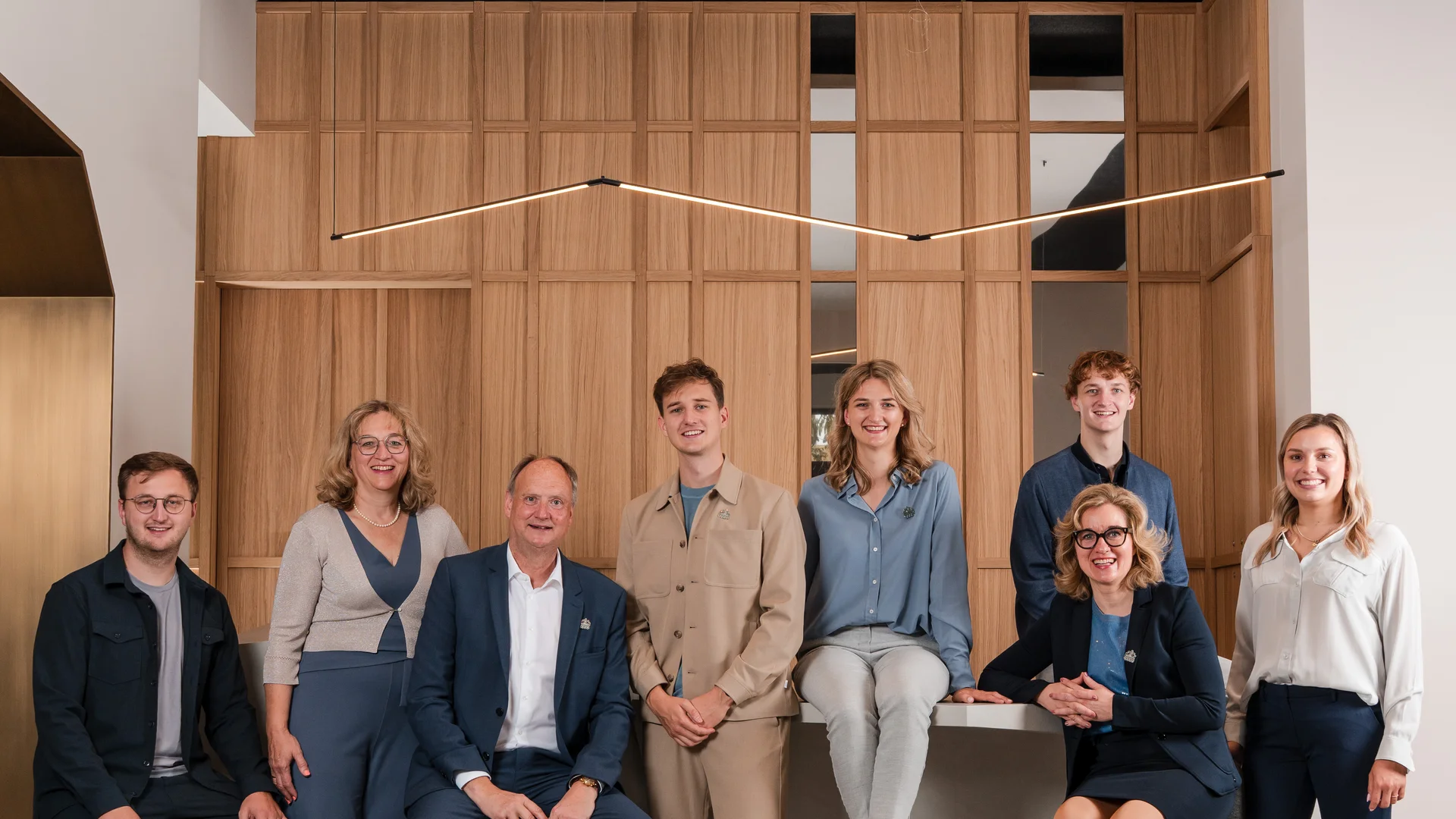 Ihre Gastgeber im Cervus Gruppenfoto von acht Personen vor einer Holzpaneelwand in modernem Büro