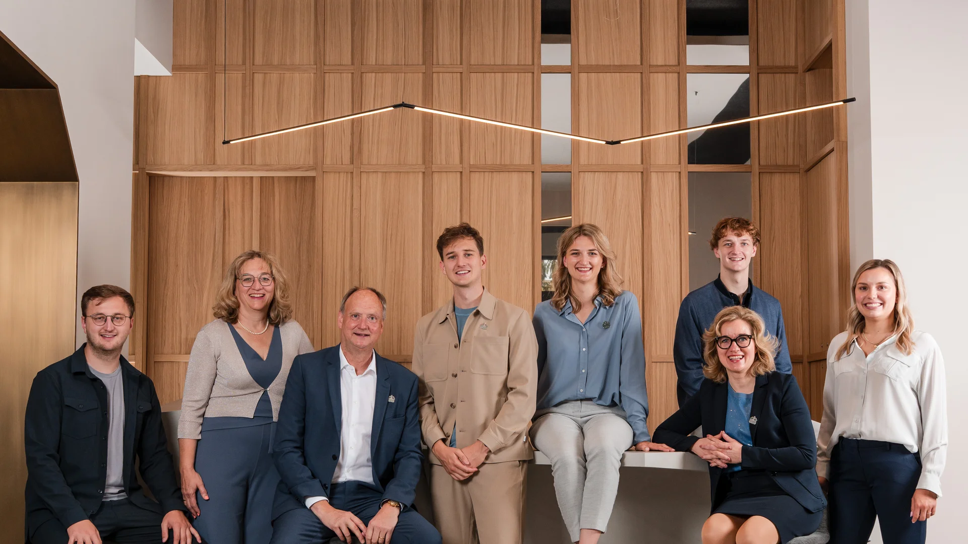 Group photo of eight people in front of a wooden panel wall in modern office