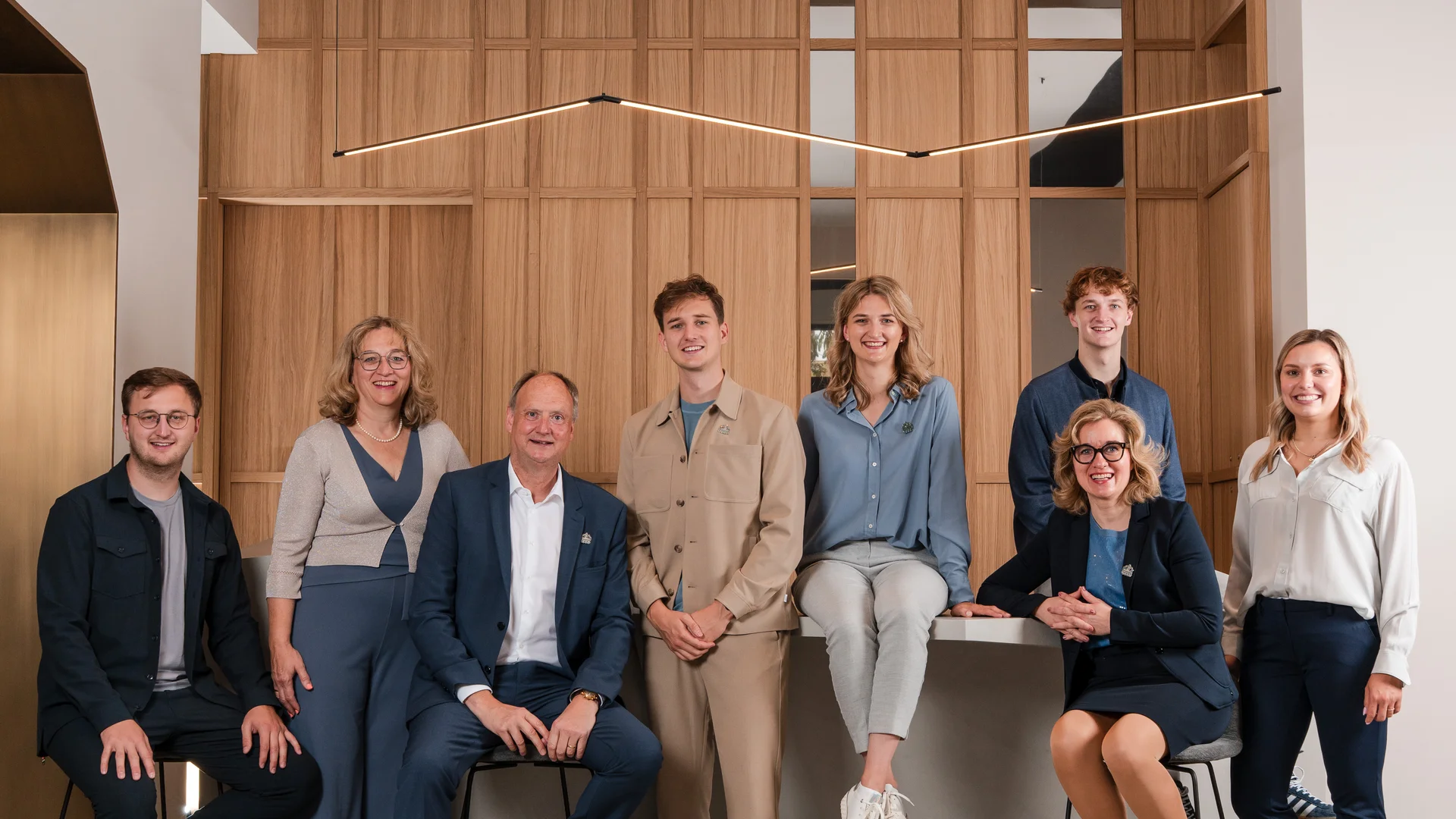 Gruppenfoto von acht Personen vor einer Holzpaneelwand in modernem Büro