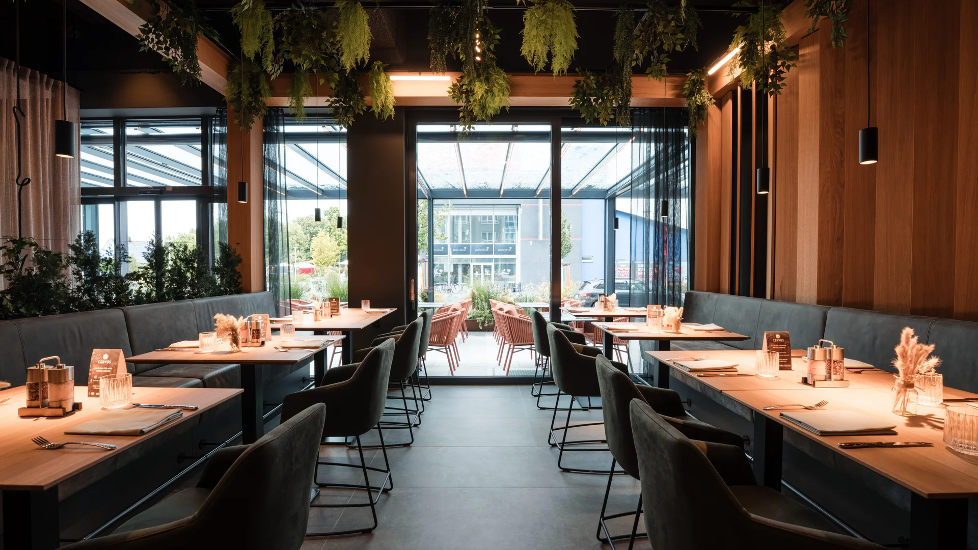 Modernes Restaurant mit Holztischen, grünen Pflanzen und großer Fensterfront