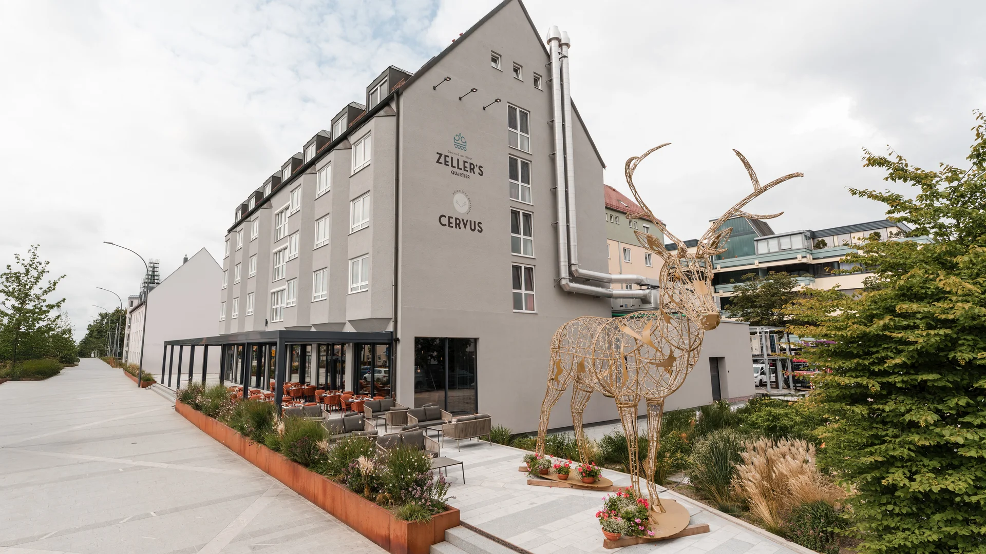 Modern building with café terrace and large wooden deer sculpture outdoors