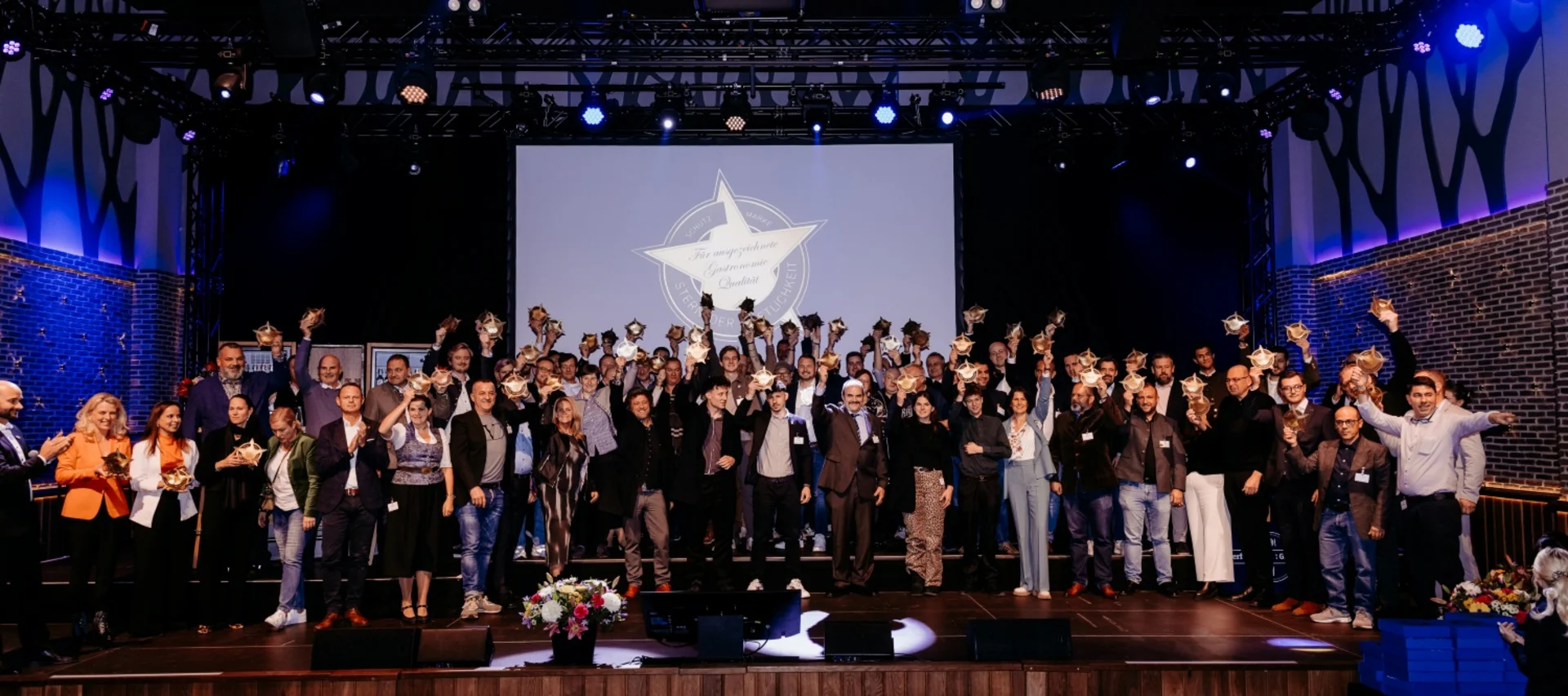 Goldener Stern Award Verleihung 2025 – Paulaner am Nockherberg, München“ Gruppenfoto der Gewinnerinnen und Gewinner der Goldener Stern Award Verleihung auf der Bühne im Paulaner am Nockherberg in München. Alle halten ihre Trophäen hoch, im Hintergrund ist eine große Leinwand mit dem Award-Logo zu sehen.“