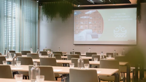 Zeller’s Quartier: das besondere Tagungshotel in Bayern Heller Tagungsraum mit grünen Stühlen und Vorhängen.