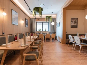 Südtiroler Stube Heller Gastraum im Restaurant Cervus mit gedeckten Holztischen, Stühlen, Sitzbänken und warmem Licht.