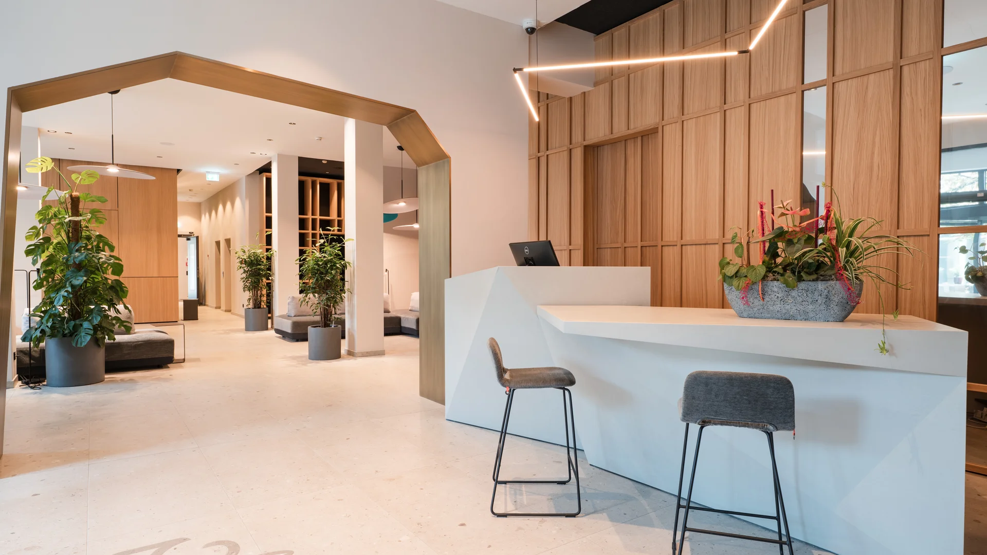 Modern reception area with white desk, two stools, and plants