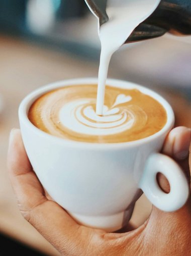 Milchschaum wird in eine Tasse Kaffee für Latte Art gegossen