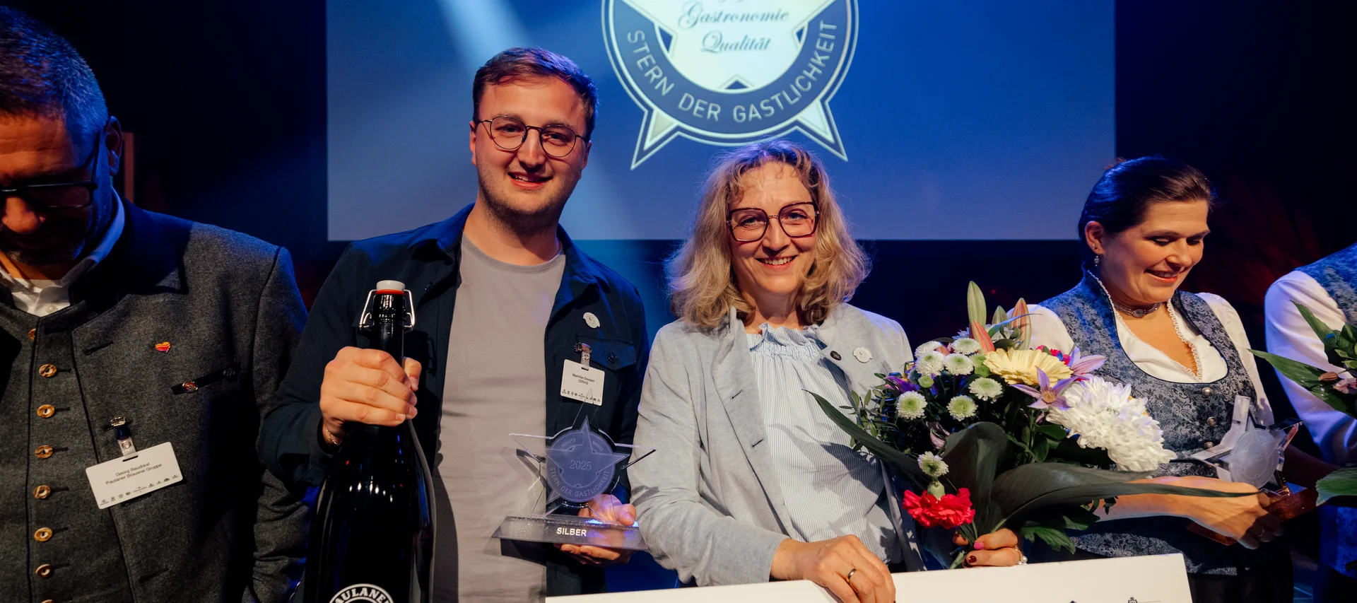 Personen erhalten Silber-Auszeichnung Stern der Gastlichkeit bei Preisverleihung mit Blumen und Urkunde